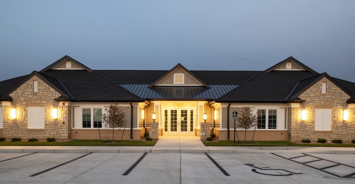 A well-lit building entrance during the evening with an empty parking lot.