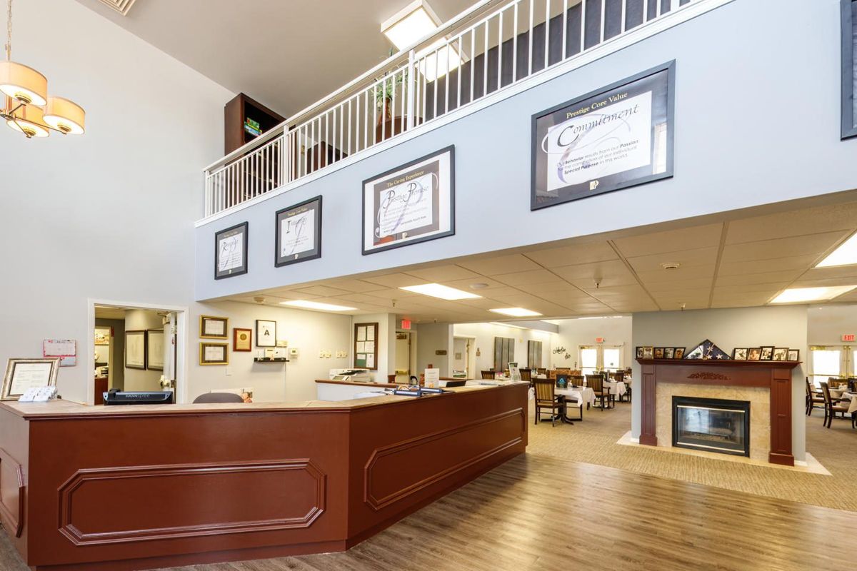 A spacious and well-lit office reception area featuring a wooden desk, certificates on the walls, and an open upstairs balcony.