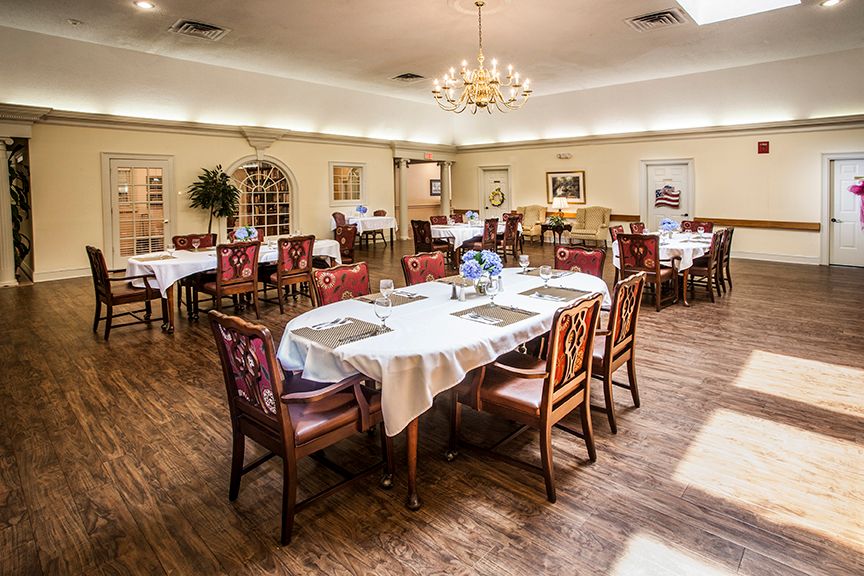 An elegant dining room setup with tables and chairs, featuring a chandelier and wooden flooring.