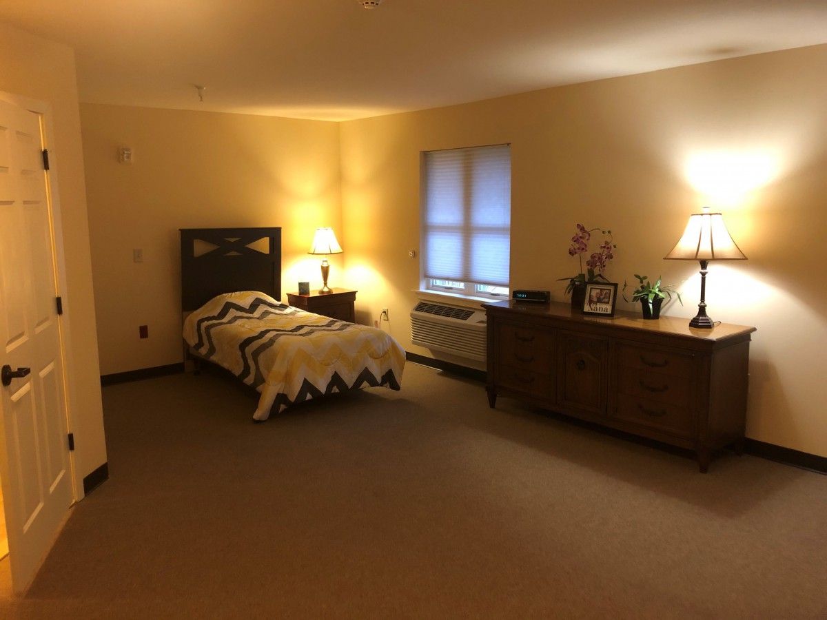 A cozy bedroom featuring a single bed, two lamps, and a wooden dresser.