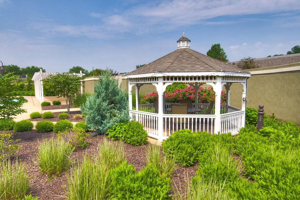A charming white gazebo surrounded by lush greenery in a landscaped garden under a clear blue sky.