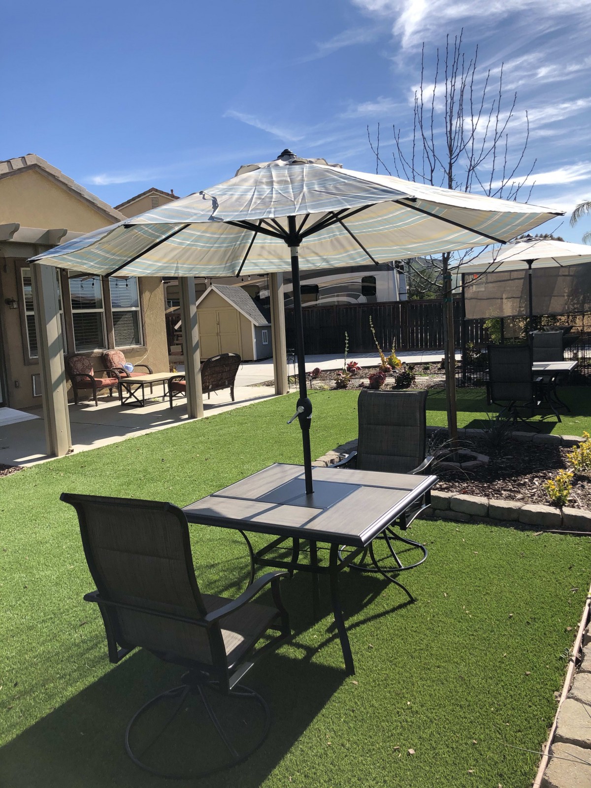 A backyard patio with a table, chairs, and an open umbrella on a sunny day.