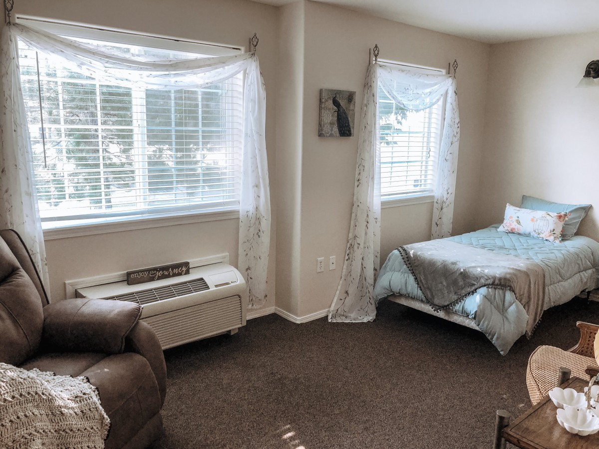 A cozy bedroom with a bed, chair, and large windows draped with curtains.