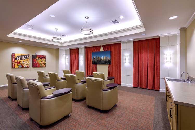 A cozy theater room with comfortable armchairs arranged in front of a large TV, surrounded by elegant red curtains and soft lighting.