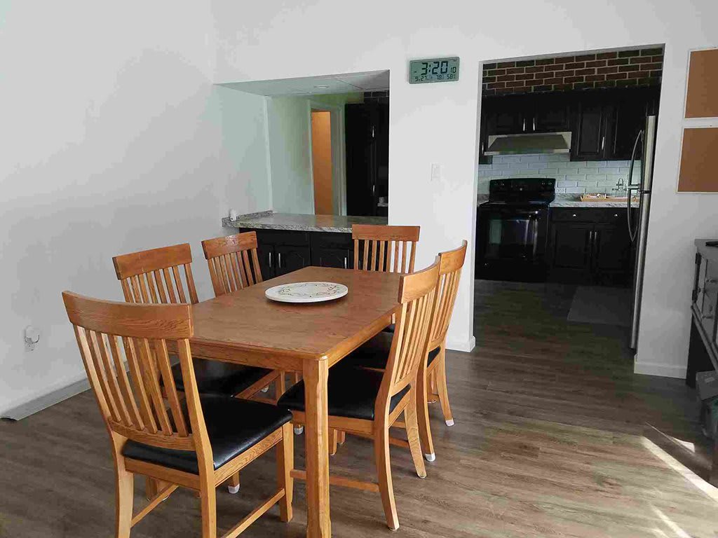 A modern dining area featuring a wooden table and chairs, leading into a sleek kitchen.