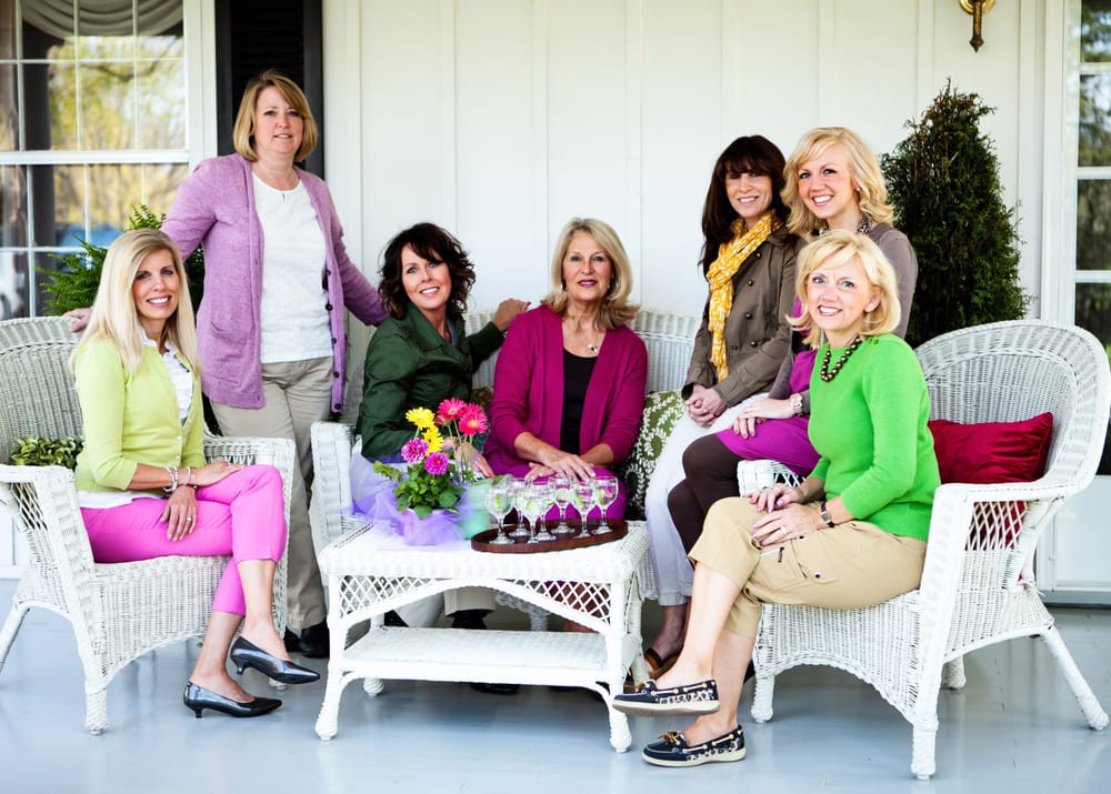 A group of women sitting on a porch, dressed in casual and colorful attire.