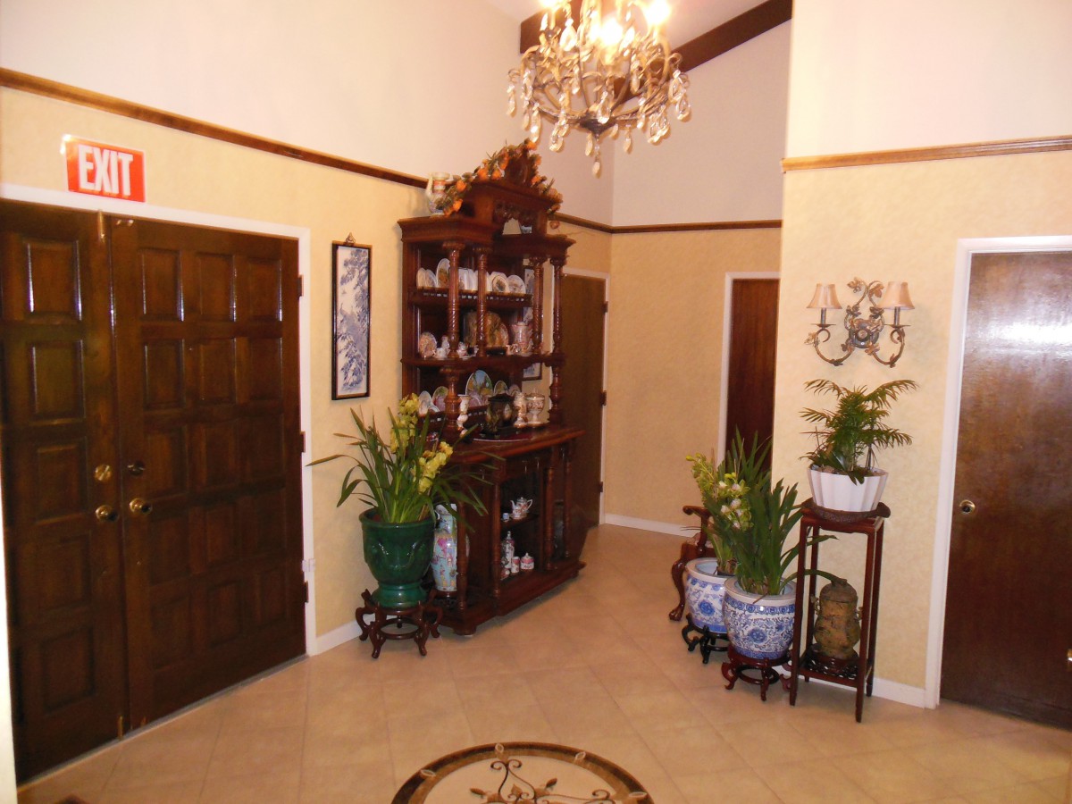A well-decorated hallway with a chandelier, plants, and wooden furniture accentuating its elegance.