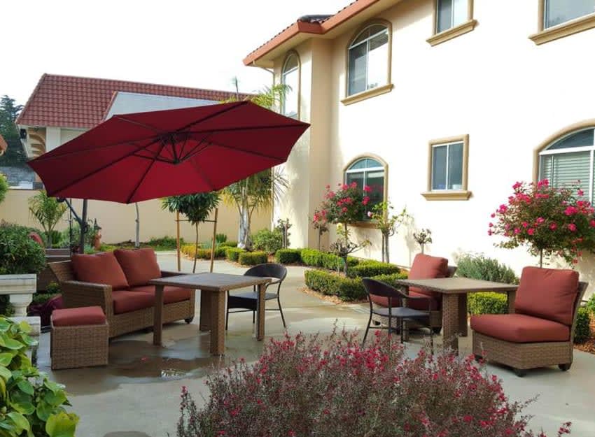 A cozy outdoor patio area with comfortable seating and a red umbrella, set against the backdrop of a well-maintained garden and house.