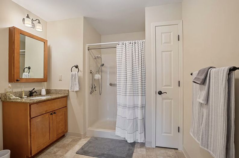 A modern bathroom with a shower enclosed by a striped curtain, a wooden vanity, and tile flooring.