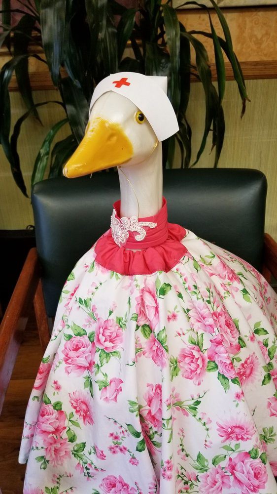 A decorative goose dressed in a floral outfit with a bonnet, sitting on a chair.