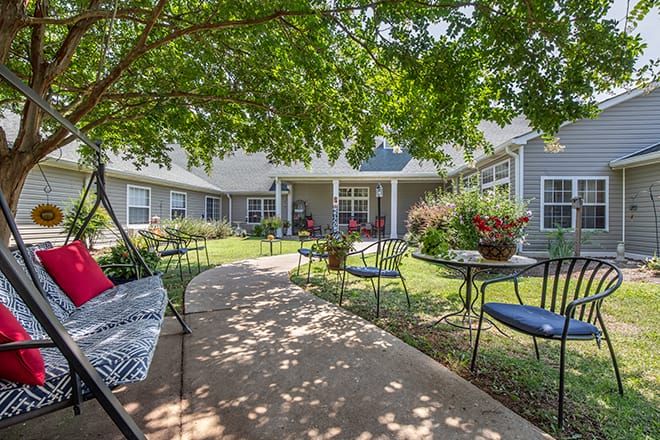 A tranquil garden patio with tables and chairs under the shade of lush trees.