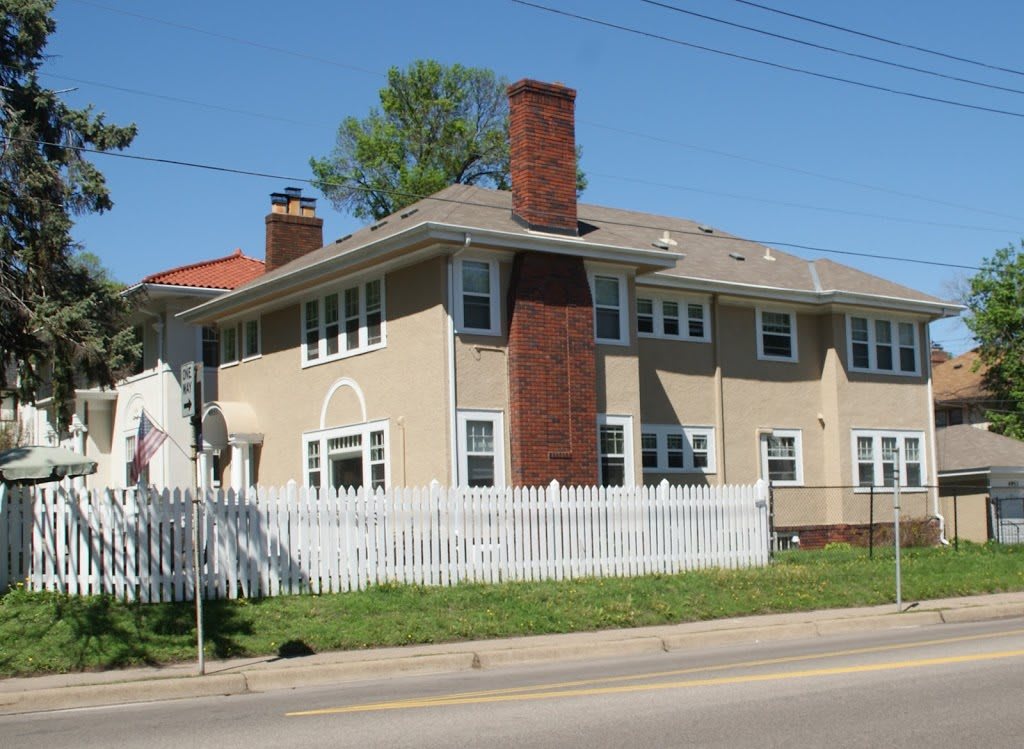 A two-story residential house with a white picket fence and prominent chimneys.