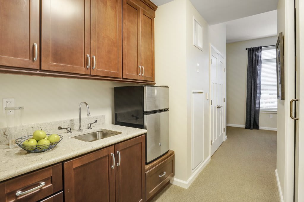 A modern apartment kitchenette with wooden cabinets and a compact refrigerator.