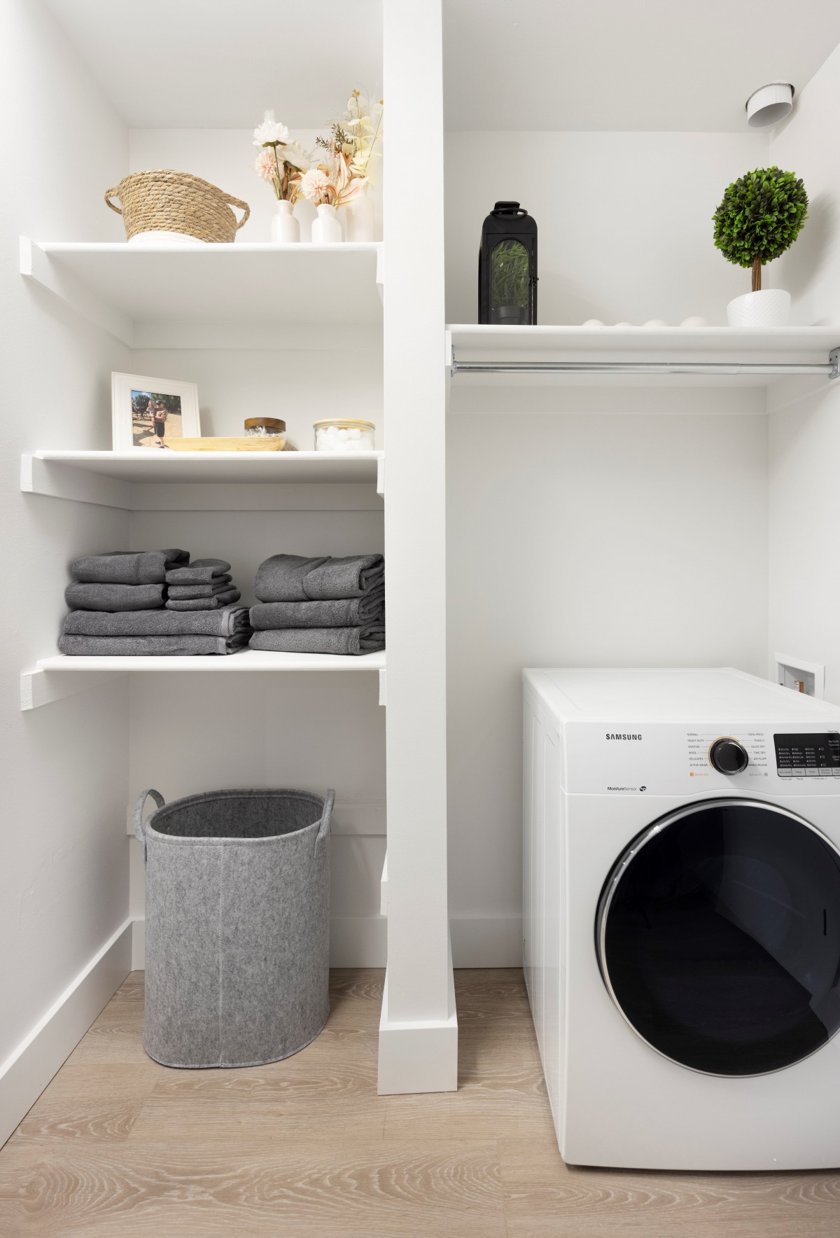 A neat and organized laundry room with a washing machine, shelves with folded towels, and a laundry basket.