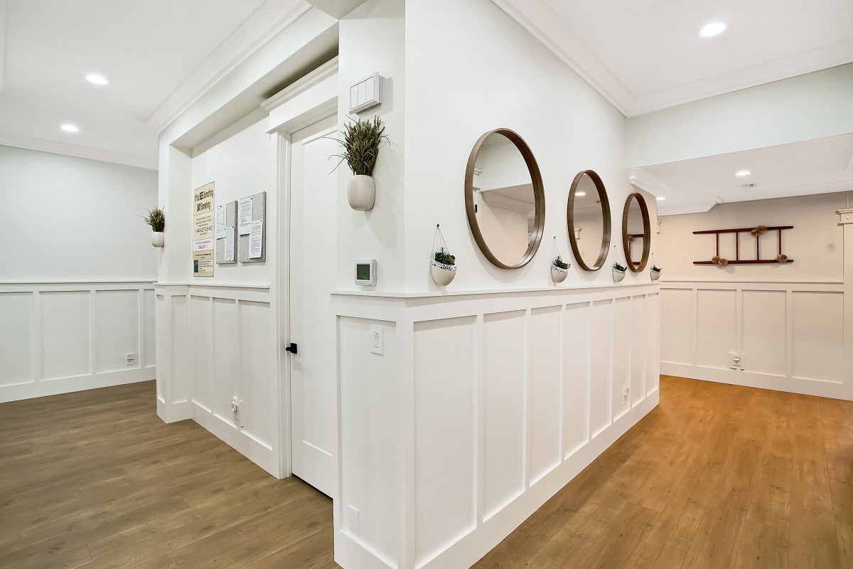 A modern hallway with white wainscoting and multiple round mirrors on the wall, complemented by wood flooring.