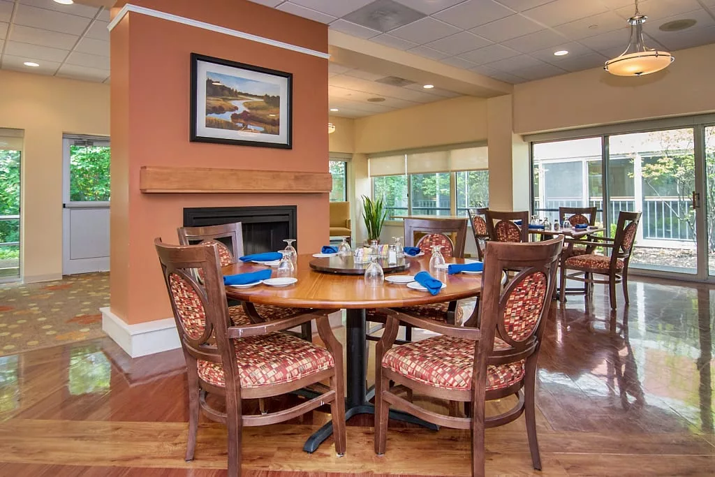 A cozy dining area with elegantly set tables, featuring a warm fireplace and artistic decor.