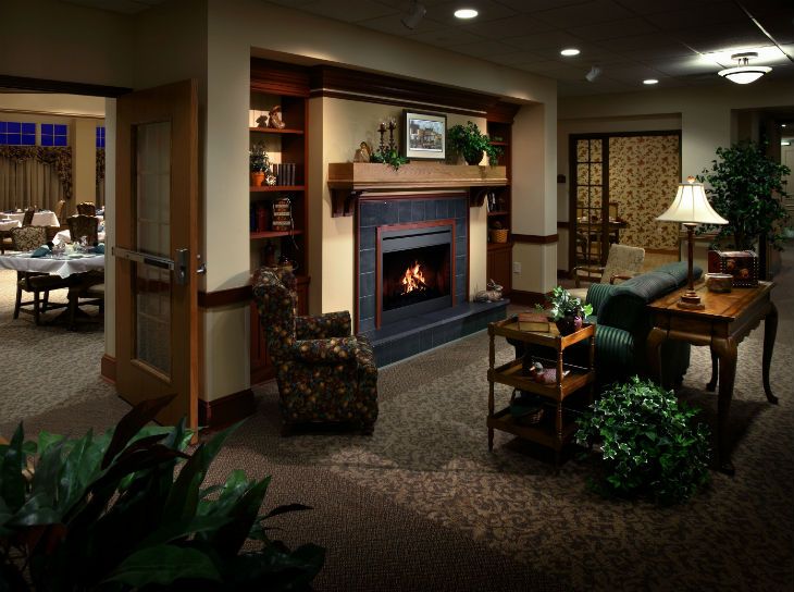 A cozy living room with a fireplace, armchair, and bookshelf.