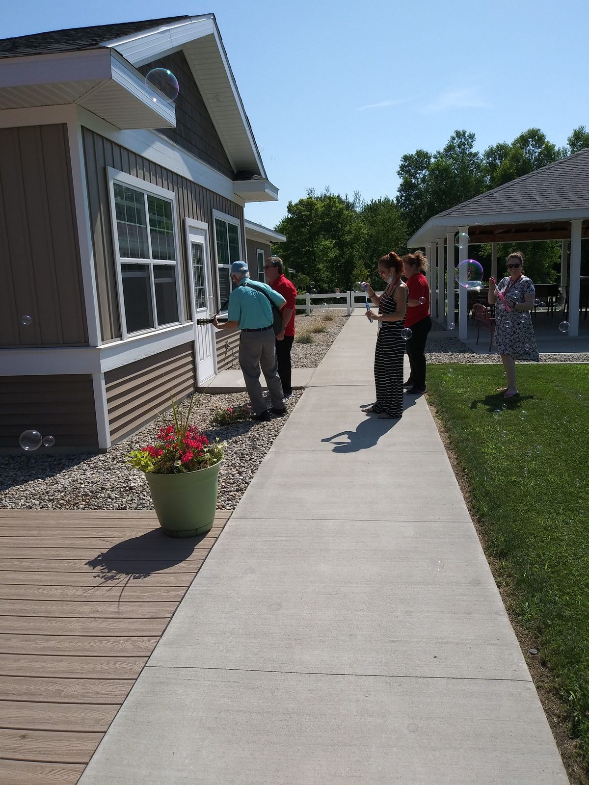 A group of people standing on a sidewalk next to a building and garden on a sunny day.