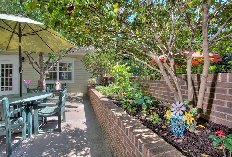 A serene garden patio with outdoor furniture surrounded by lush greenery and a brick wall.