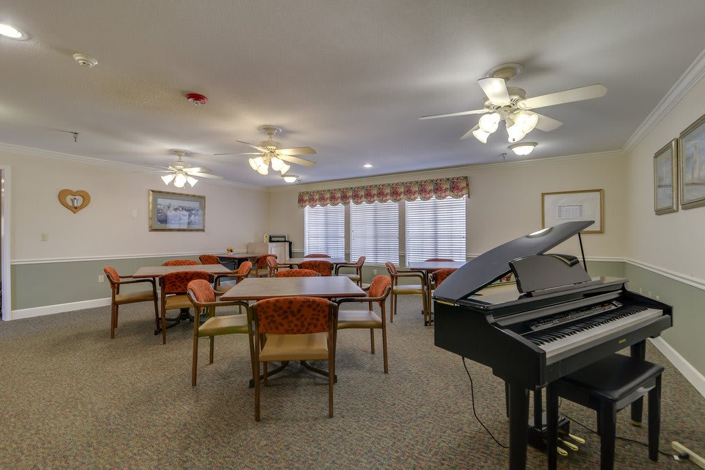 A well-lit room with tables, chairs, a piano, and ceiling fans.