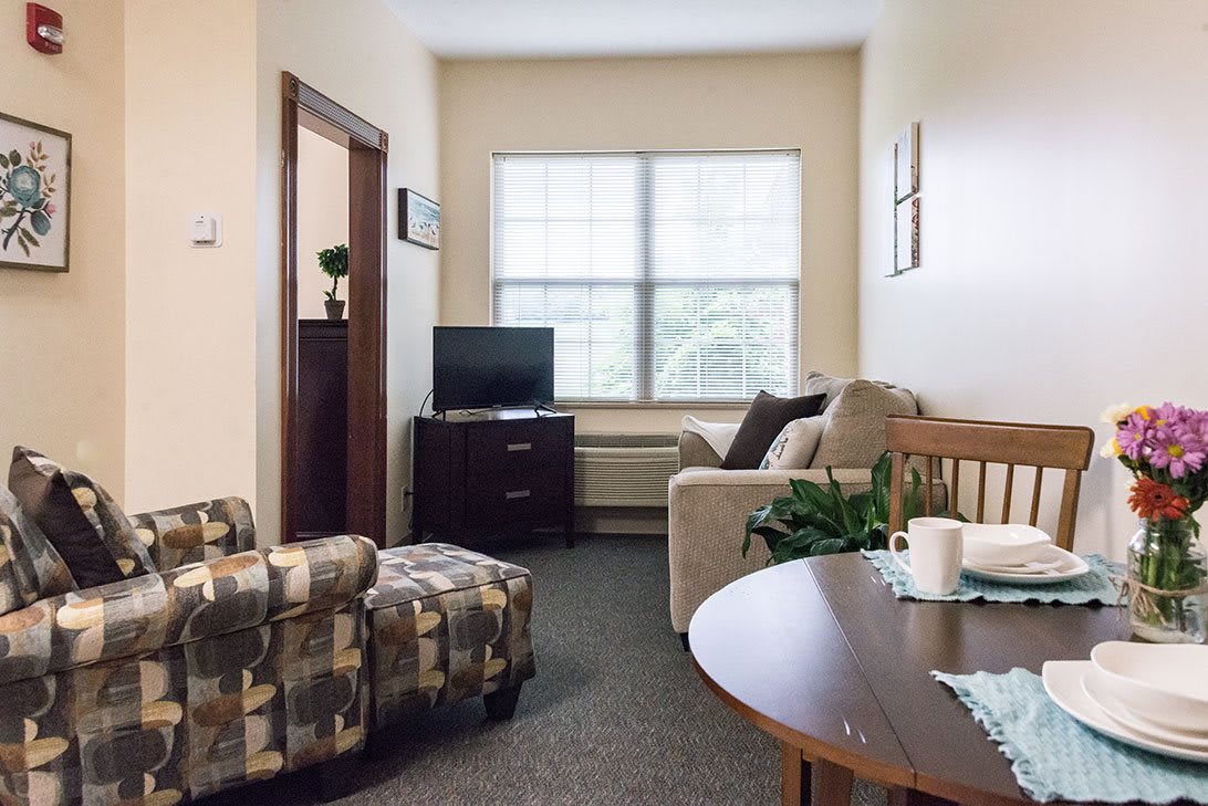A cozy living room with a sofa, armchair, and a television by the window.