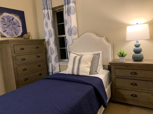 A cozy bedroom with a single bed, adorned with blue and white bedding, a nightstand with a lamp, and matching dressers.