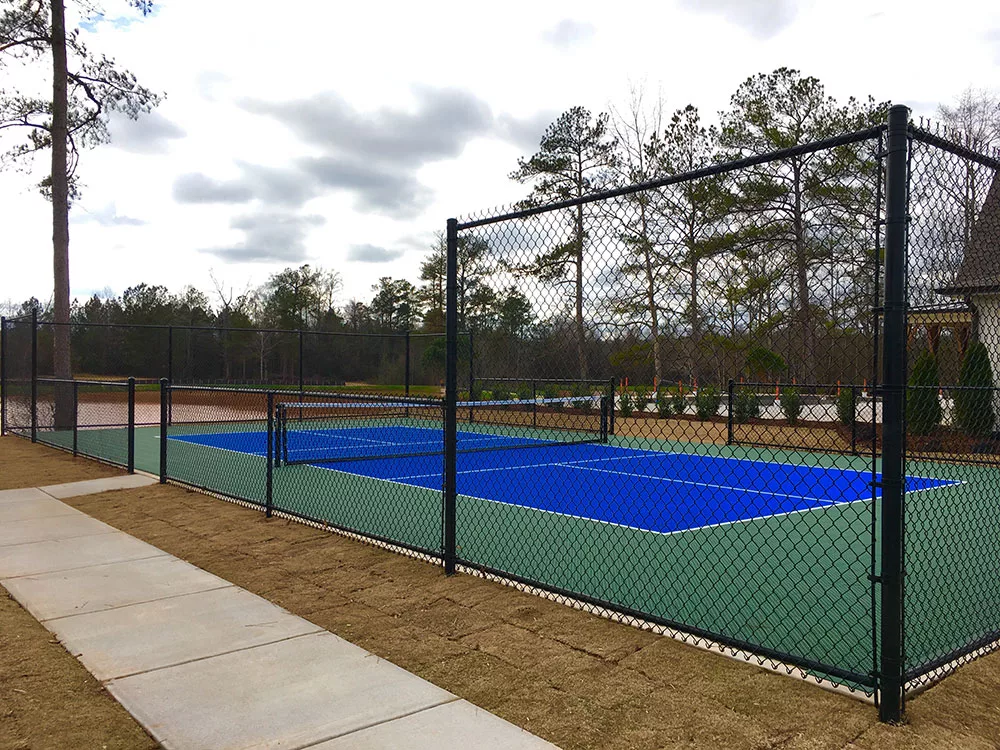 An outdoor tennis court surrounded by a fence, set against a backdrop of trees.