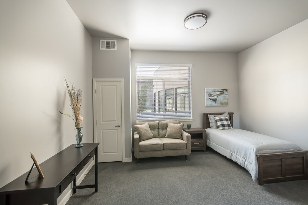 A modern, minimalist bedroom with neutral colors featuring a single bed and sofa.