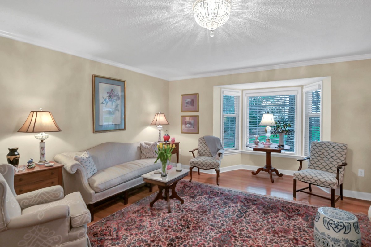 A cozy living room with traditional decor, featuring a chandelier, upholstered seating, and a large window.