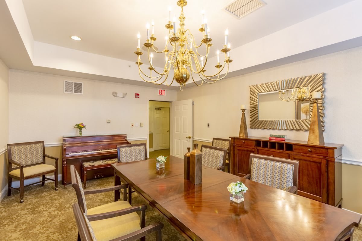 A well-furnished dining room featuring a wooden table, chairs, a chandelier, and a piano in the corner.
