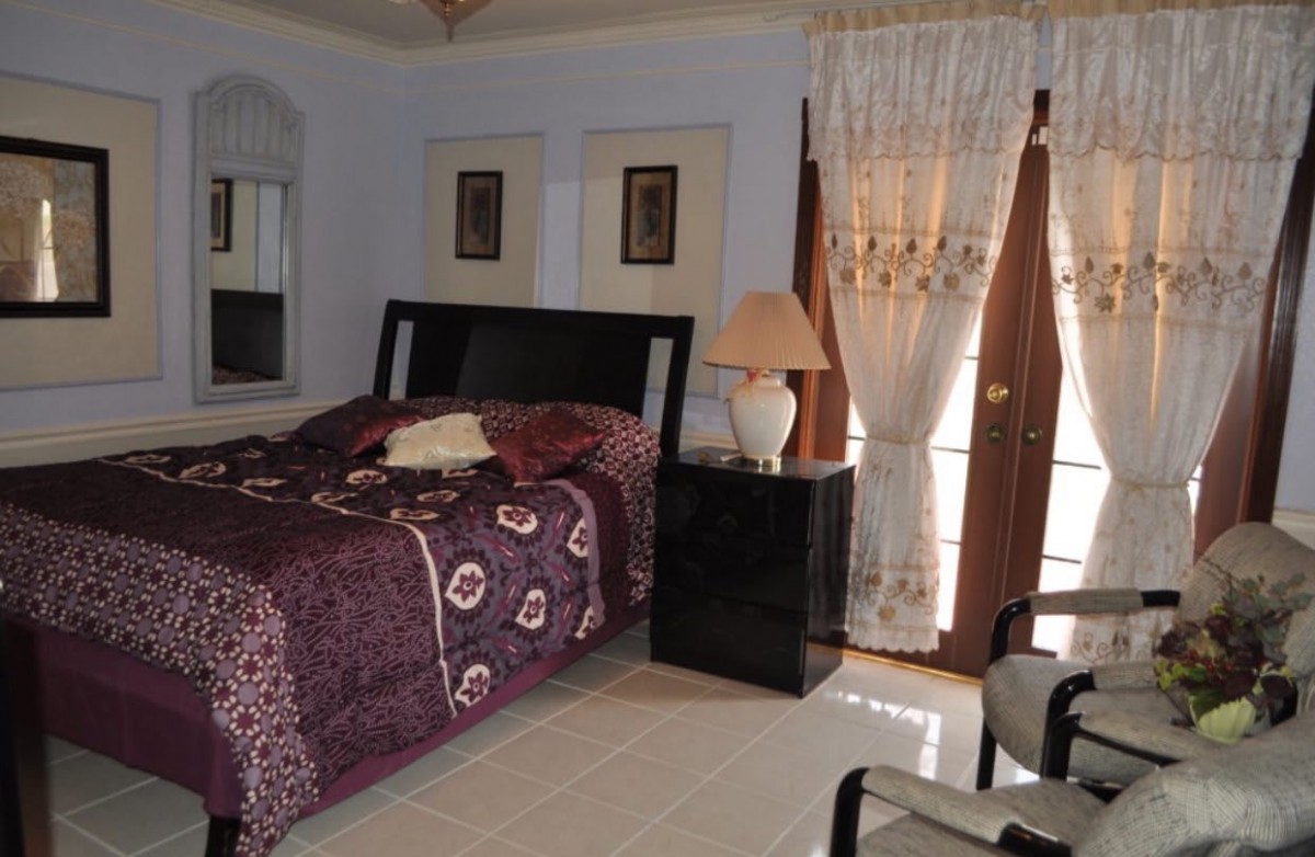 A cozy bedroom with a neatly made bed, nightstand, lamp, and decorative curtains.