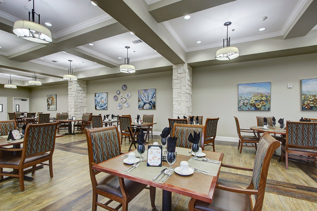 A formal dining area with neatly arranged tables and chairs, decorated with artwork and elegant lighting.