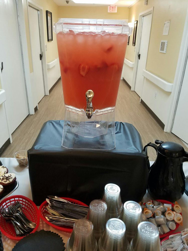 A drink dispenser filled with a red beverage is set up in a hallway, accompanied by snacks and condiments.