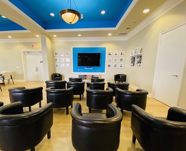 A modern lounge area with comfortable chairs facing a television, featuring a blue accent ceiling.