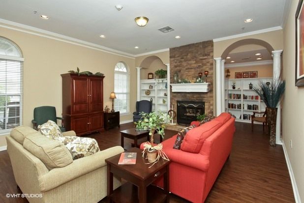 A cozy living room featuring a red sofa and beige couch, with a fireplace surrounded by bookshelves and a hardwood floor.