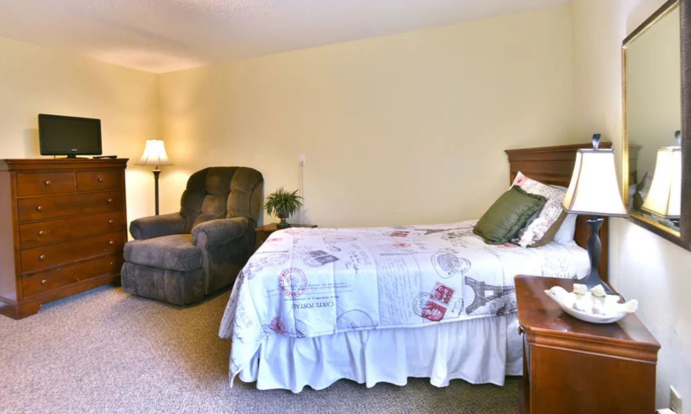 A cozy bedroom with a bed, armchair, and a lamp.