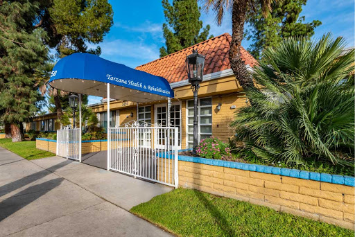 A welcoming entrance to a charming residential building, featuring a blue canopy and lush landscaping.