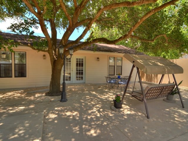 A cozy patio with a large tree providing shade, featuring a swing and outdoor furniture.