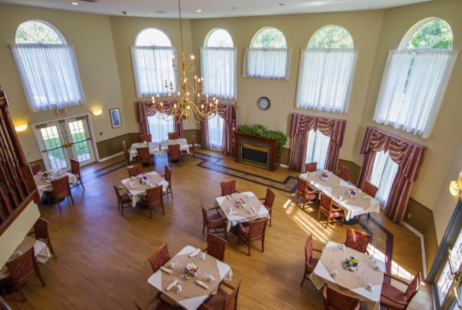 A spacious and elegantly decorated dining room with multiple tables, chandeliers, and large windows.