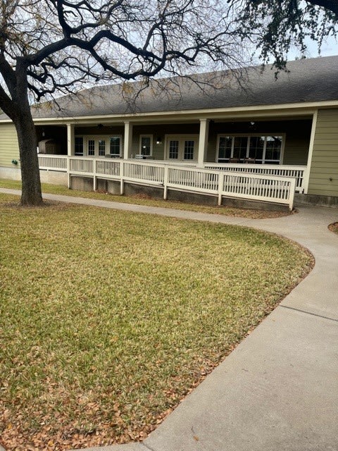 A single-story building with a ramp leading to the entrance, surrounded by grass and a tree.