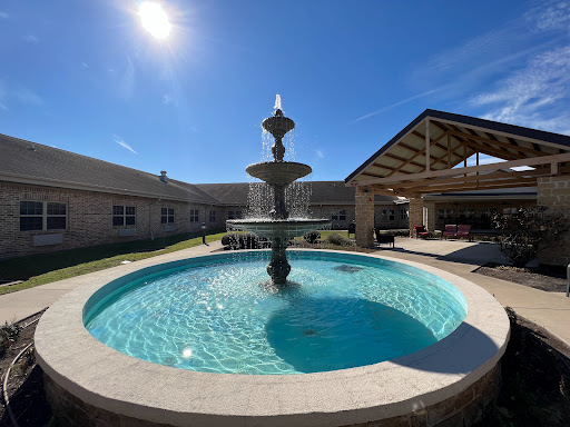 A serene outdoor space featuring a beautiful fountain surrounded by a sparkling pool under the bright sun.