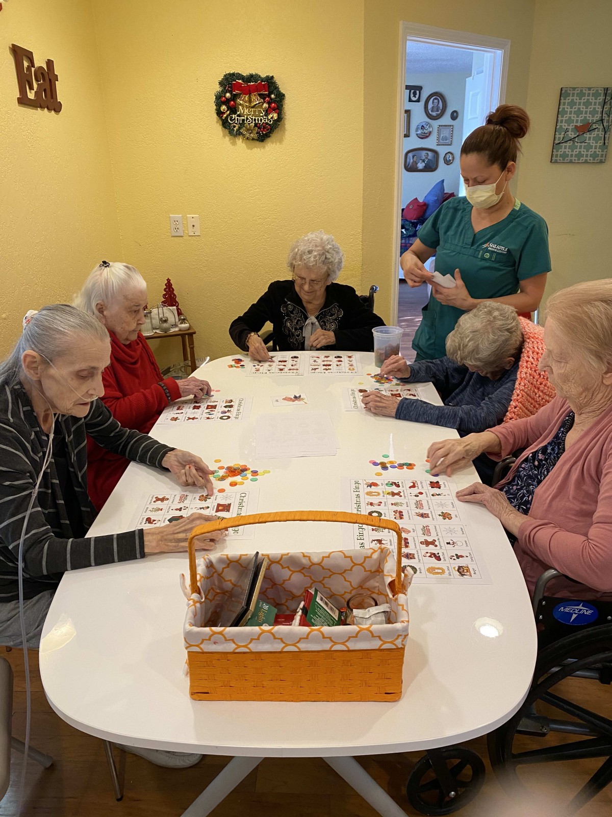 A group of elderly individuals engaged in an activity at a table, with a caregiver nearby.
