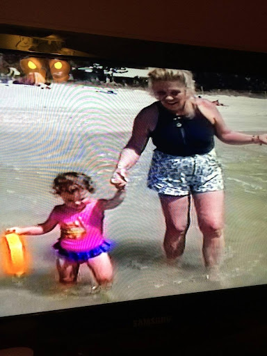 A joyful moment at the beach, where a mother is walking hand-in-hand with her young daughter as they play in the water.