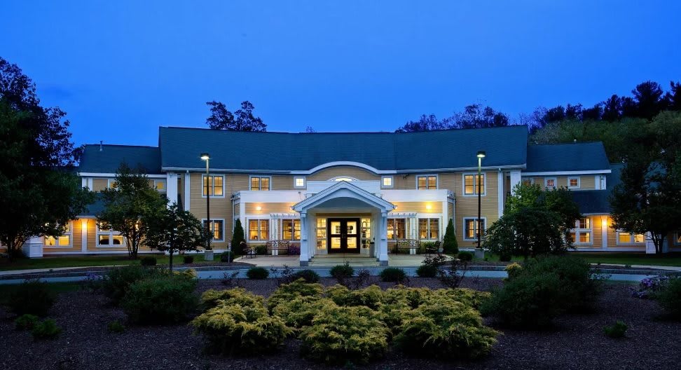 A well-lit building with a symmetrical entrance surrounded by landscaped gardens during the evening.