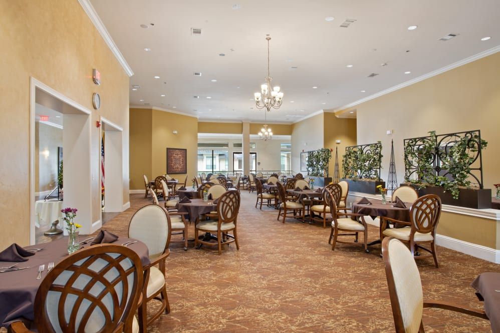 An elegant and spacious dining room with multiple tables and chairs, featuring a chandelier and warm lighting.
