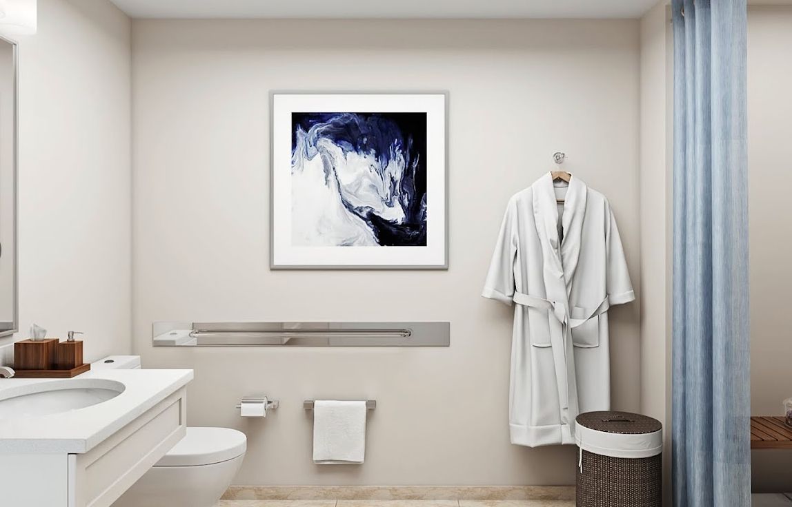 A modern minimalist bathroom featuring a framed abstract artwork and a hanging robe.