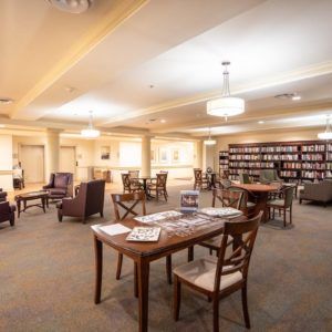 A well-lit library reading area with tables, chairs, and bookshelves.