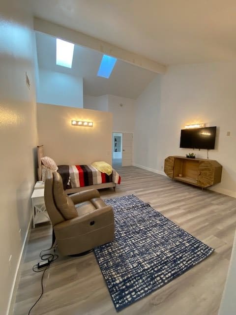 A modern living room with a cozy armchair, sofa, and wall-mounted TV.
