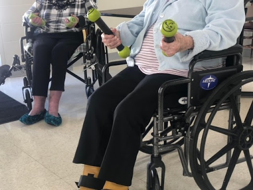 Seniors participating in a fitness class using small weights from their wheelchairs.