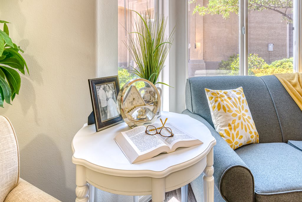 A cozy living room corner with a decorative side table, featuring an open book, glasses, and a framed photo.